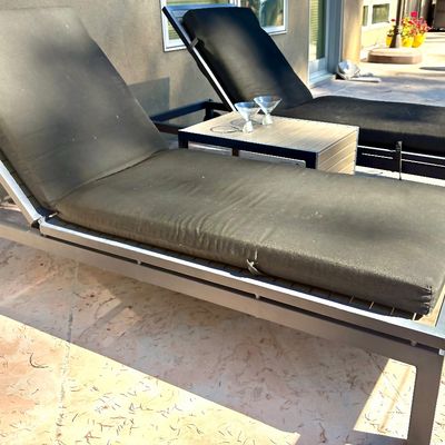 Pair of modern outdoor chaise lounges with dark grey cushions and a matching slatted-top side table.