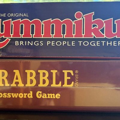 A stack of two classic board games, featuring Pressman Rummikub Classic and a Scrabble Crossword Game in its original shrink wrap.