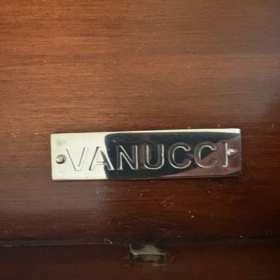 Vanucci maker's mark plaque in polished metal, mounted on a dark wood surface.