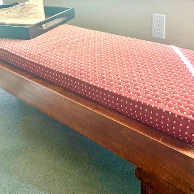 Rustic wooden bench featuring a thick, patterned red cushion and sturdy block legs, topped with a black serving tray.