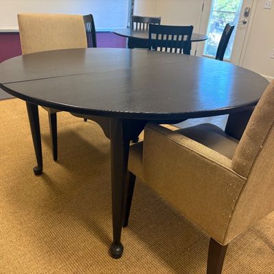 Dark wood round dining table with tapered legs, paired with two upholstered tan armchairs.