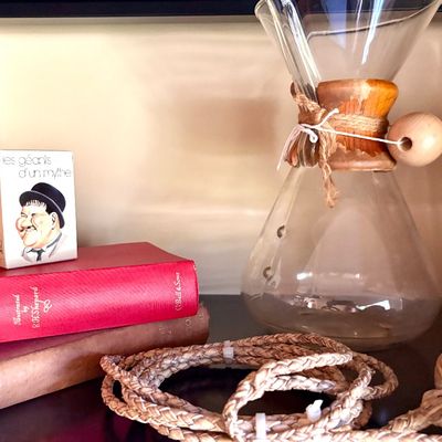 Vintage Chemex glass coffee maker with a wooden collar and leather tie, displayed alongside vintage books and a small Oliver Hardy...