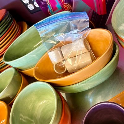 Assorted colorful ceramic tableware, including green and orange bowls, plates, and a bag of matching napkin rings.
