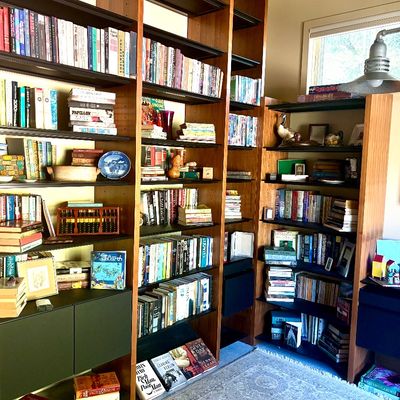 Large modular wooden shelving unit filled with books, decorative plates, and small collectibles, featuring integrated dark green and blue...