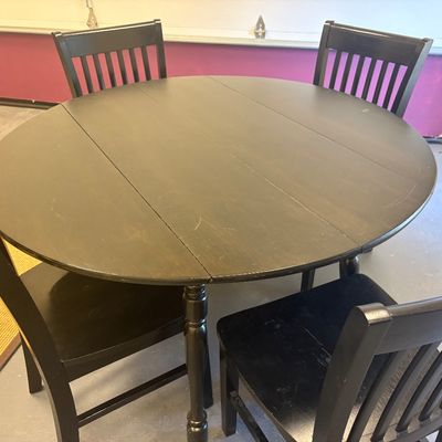 Contemporary black-finished wooden dining set featuring a round drop-leaf table and four matching slat-back chairs.