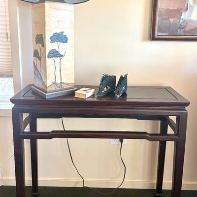 Asian-style dark wood console table featuring a rectangular top, straight legs, and a lower stretcher bar, styled with a tall painted...