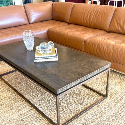 Contemporary tan leather sectional sofa with tufted seat cushions, paired with a dark stone-top coffee table on a metal frame.