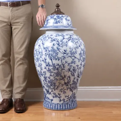 Large Chinese blue and white porcelain ginger jar with a matching lid topped by a bronze-tone finial, standing next to a person for scale.