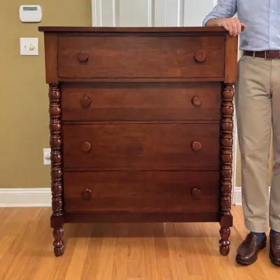 Sheraton-style cherry wood four-drawer chest featuring spool-turned corner columns and matching wooden knobs.