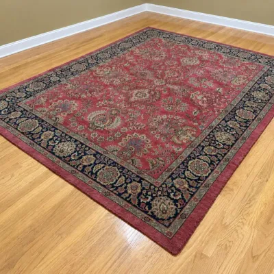 Large Persian-style area rug featuring a red field with intricate floral motifs and a dark navy blue border, shown on a hardwood floor.
