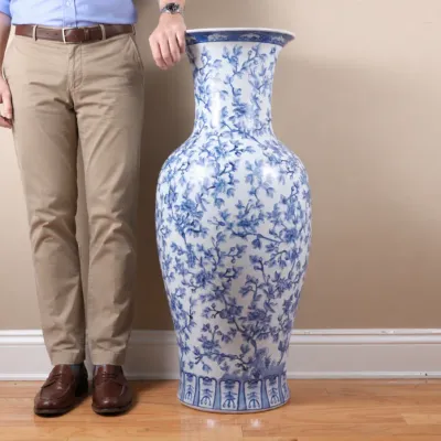 Large Chinese blue and white porcelain floor vase featuring an intricate floral and vine motif, shown next to a person for scale.