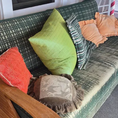 Sale Photo Thumbnail #18: Mid-century wooden-framed sofa with green textured upholstery, styled with an assortment of vintage throw pillows in green, orange, peach, and brown.