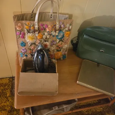 Sale Photo Thumbnail #47: Vintage woven straw tote bag with colorful embroidered flowers, shown alongside a green leather handbag, a vintage clothes iron, and a green folder on a wooden table.
