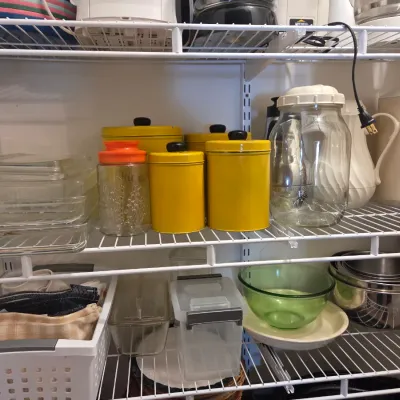 Sale Photo Thumbnail #69: Assorted kitchenware on wire shelving, including yellow metal canisters, glass baking dishes, a green glass bowl, and various storage containers.