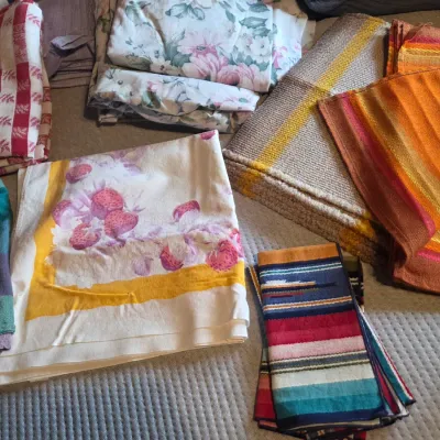 Sale Photo Thumbnail #70: Assortment of vintage linens and textiles, including floral sheets, a strawberry-patterned tablecloth, and colorful woven blankets.