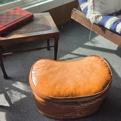 Sale Photo Thumbnail #22: Vintage kidney-shaped vinyl ottoman in tan, paired with a wooden side table featuring a cane insert and a wooden checkerboard box.