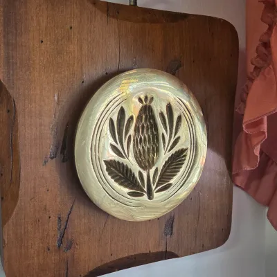 Sale Photo Thumbnail #26: Vintage brass butter mold plaque featuring a thistle design, mounted on a rustic wooden board with a hanging ring.