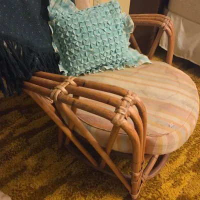 Sale Photo Thumbnail #52: Vintage mid-century bamboo or rattan swivel rocker chair with striped cushions, accompanied by a blue textured throw pillow and a dark fringed blanket.