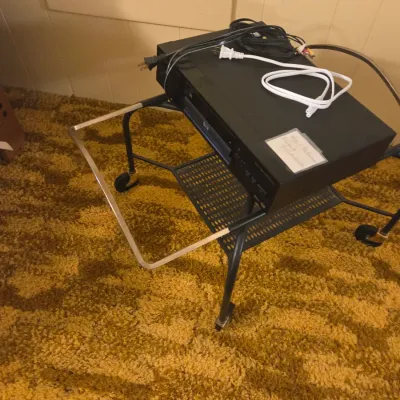 Sale Photo Thumbnail #48: Black Sony DVD player with power and AV cords, resting on a black metal rolling cart.