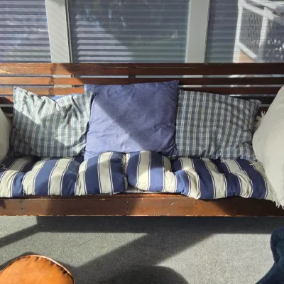 Sale Photo Thumbnail #24: Vintage wooden porch swing with a slatted back, featuring blue and white striped cushions and coordinating throw pillows.