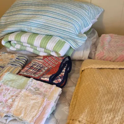 Sale Photo Thumbnail #33: Assortment of vintage and modern bedding, including a yellow fringed coverlet, a patchwork rag quilt, and striped quilted blankets.