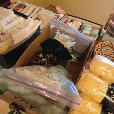 Sale Photo Thumbnail #49: Assorted crafting and sewing supplies, including skeins of yellow yarn, vintage lace trim in plastic bags, and folded fabrics in boxes.