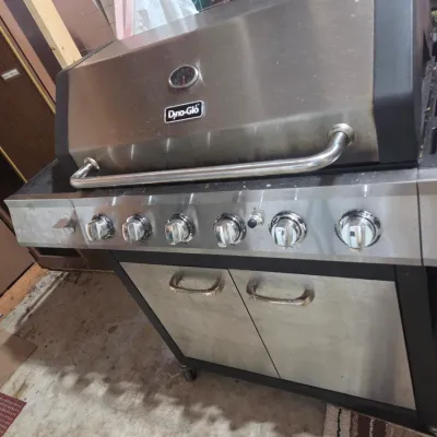 Sale Photo Thumbnail #3: Dyna-Glo stainless steel five-burner gas grill with a built-in temperature gauge and lower storage cabinet.