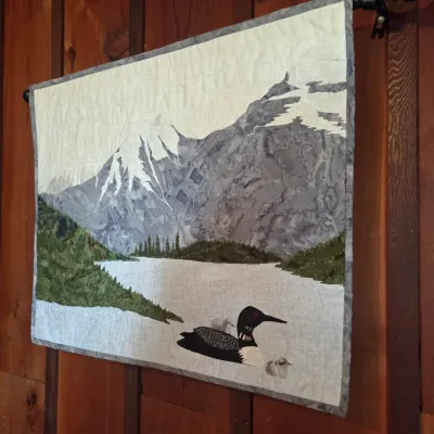 Sale Photo Thumbnail #75: Handcrafted quilted wall hanging depicting a loon on a mountain lake, featuring detailed applique work and textured stitching.