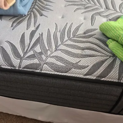 Sale Photo Thumbnail #64: Modern mattress featuring a grey and white palm leaf pattern with a dark grey ribbed border, shown with folded blankets on top.