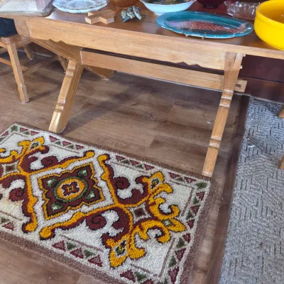 Sale Photo Thumbnail #83: Vintage latch hook rug featuring a bold geometric and scroll pattern in yellow, brown, and red, displayed on a wood floor next to a rustic wooden dining set.