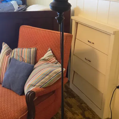 Sale Photo Thumbnail #37: Vintage orange upholstered armchair with wooden arm accents, paired with a black metal floor lamp and a white four-drawer chest.