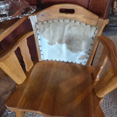 Sale Photo Thumbnail #90: Rustic oak armchair featuring a cowhide-upholstered backrest with decorative nailhead trim and a carved handle grip.
