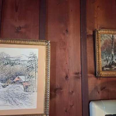 Sale Photo Thumbnail #72: Two framed winter landscape artworks, including a print of a covered bridge and a small oil painting of a snowy forest, both in ornate gold-finished frames.