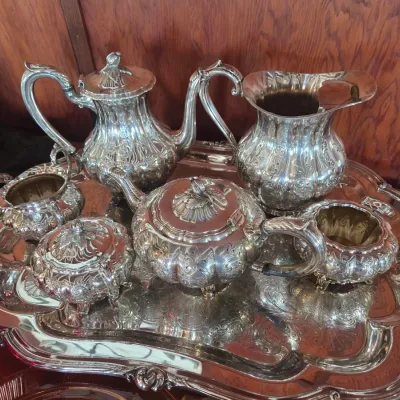 Sale Photo Thumbnail #89: Ornate silver-plated tea and coffee service set, featuring a teapot, coffee pot, creamer, sugar bowl, and waste bowl on a matching footed serving tray with repoussé floral details.