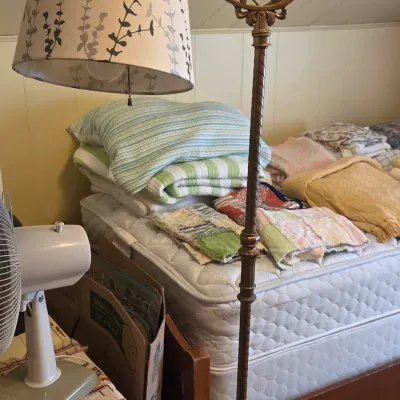 Sale Photo Thumbnail #35: Vintage brass bridge floor lamp with an ornate scroll arm and a patterned fabric shade, shown alongside a bed stacked with various quilts and blankets.