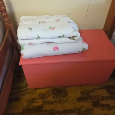 Sale Photo Thumbnail #43: Vintage pink-painted wooden storage chest or toy box, topped with folded white blankets featuring a pink floral pattern.