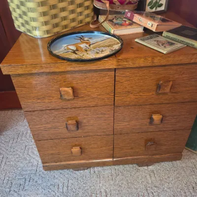 Sale Photo Thumbnail #73: Vintage oak six-drawer chest with square wooden pulls, topped with a metal picnic basket, a decorative tray featuring a pronghorn antelope, and various vintage books.