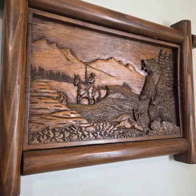 Sale Photo Thumbnail #60: Hand-carved wooden relief plaque depicting a rustic wilderness scene with a hunter on horseback, a bear, and a deer, set in a log-style frame.