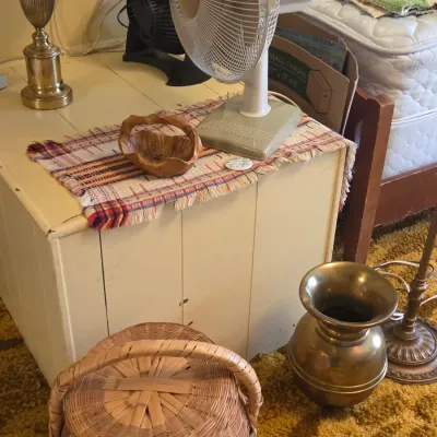 Sale Photo Thumbnail #36: Vintage white-painted wooden storage chest topped with a small woven runner, a carved wooden basket, and a vintage white oscillating desk fan, shown alongside a brass spittoon and a woven wicker basket.
