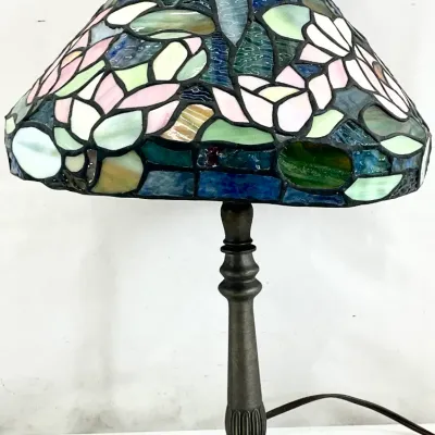 Sale Photo Thumbnail #101: Tiffany-style table lamp featuring a stained glass shade with a floral motif in shades of blue, green, and pink, mounted on a dark bronze-finished metal base.