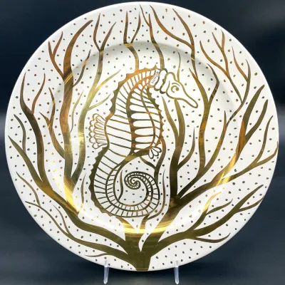 Sale Photo Thumbnail #50: Jonathan Adler ceramic plate featuring a metallic gold seahorse and seaweed design on a white background.
