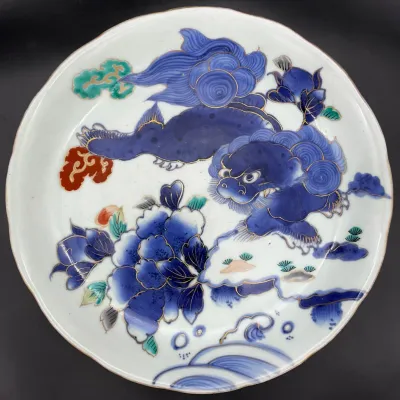 Sale Photo Thumbnail #78: Japanese Arita porcelain plate featuring a hand-painted blue Shishi (foo dog) and peony design with gold gilt accents.