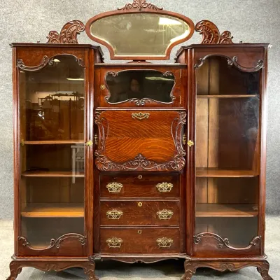 Sale Photo Thumbnail #57: Antique Victorian oak side-by-side secretary desk and bookcase cabinet, featuring ornate wood carvings, a drop-front desk, three lower drawers with brass pulls, and a top-mounted swivel mirror.