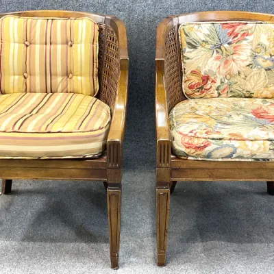 Sale Photo Thumbnail #29: Pair of vintage barrel-back cane armchairs with fluted legs, one featuring striped cushions and the other with floral patterned cushions.