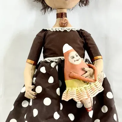 Sale Photo Thumbnail #61: Handcrafted folk art Halloween witch doll on a metal stand, featuring a polka dot dress, striped legs, and holding a small candy corn figure.