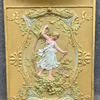 Sale Photo Thumbnail #31: Antique cast iron fireplace summer cover featuring a painted relief of Diana the Huntress with a stag, finished in gold, green, and pastel tones.