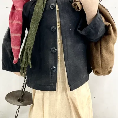 Sale Photo Thumbnail #67: Handcrafted folk art doll depicting an elderly figure or gnome, featuring a sculpted face with wire glasses, a red stocking cap, a dark jacket, and carrying a sack and a scale.