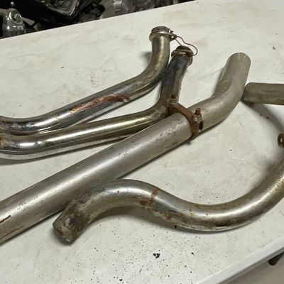 An Assortment of Four Used Motorcycle Exhaust Header Pipes and Heat Shields