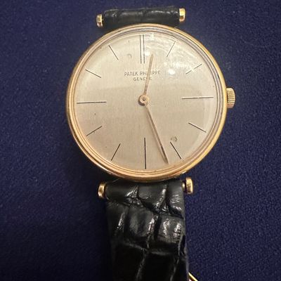 Vintage Patek Philippe Genève gold-tone dress watch featuring a minimalist silvered dial, stick hour markers, and a black...