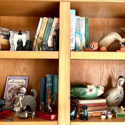 Assortment of vintage books, ceramic cat figurines, and bird sculptures displayed on a light oak wooden bookshelf.